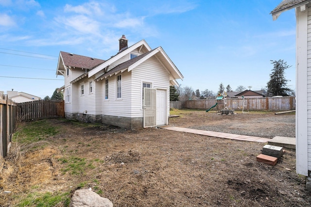 view of side of property featuring a playground, a chimney, and a fenced backyard