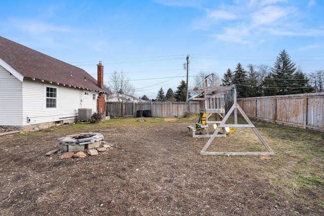 view of yard featuring central AC unit, a fenced backyard, a fire pit, and a playground