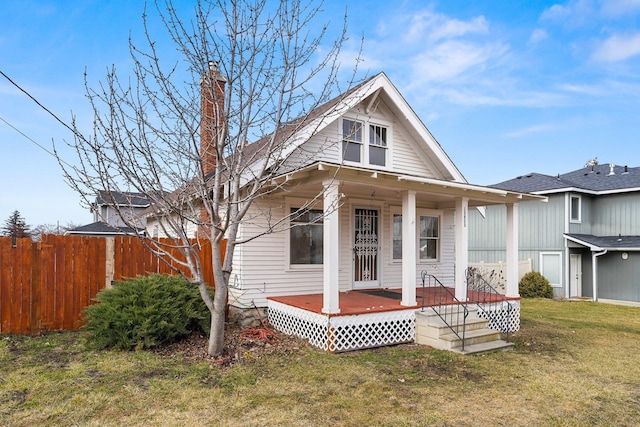 view of front of property featuring a porch, a chimney, a front yard, and fence