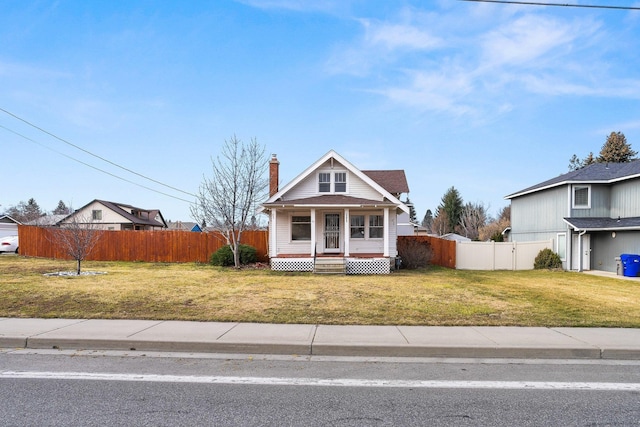 view of front facade with covered porch, a front lawn, a chimney, and fence