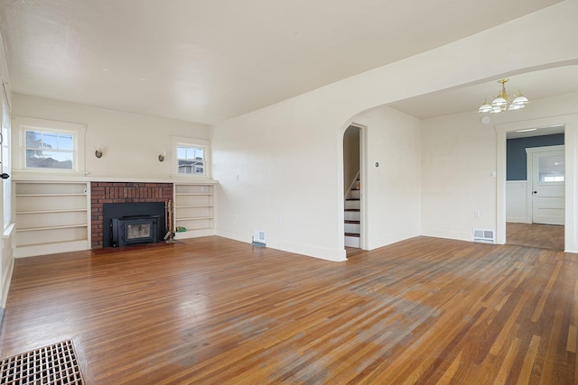 unfurnished living room featuring stairway, visible vents, arched walkways, and wood finished floors