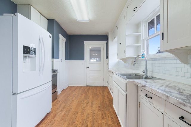 kitchen with light wood-type flooring, white fridge with ice dispenser, white cabinetry, open shelves, and a sink