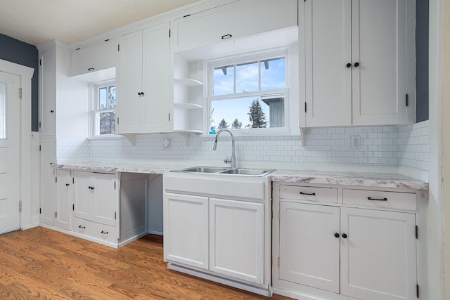 kitchen with a wealth of natural light, decorative backsplash, white cabinets, and a sink