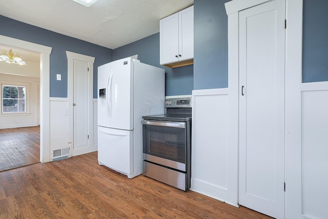 kitchen featuring white refrigerator with ice dispenser, wood finished floors, visible vents, white cabinetry, and electric stove