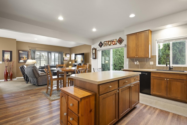 kitchen featuring dishwasher, a kitchen island, open floor plan, light countertops, and a sink