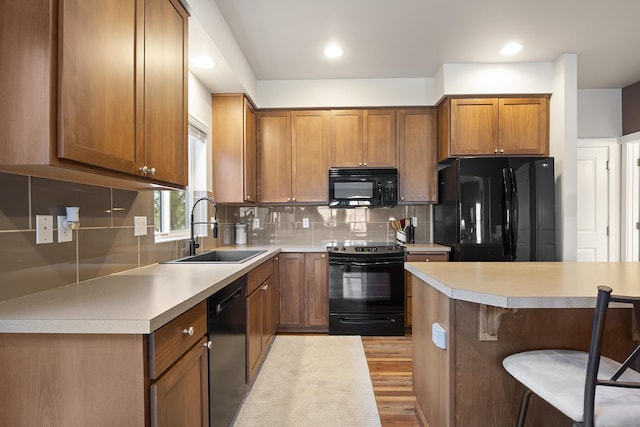 kitchen with a sink, black appliances, tasteful backsplash, brown cabinetry, and a kitchen bar