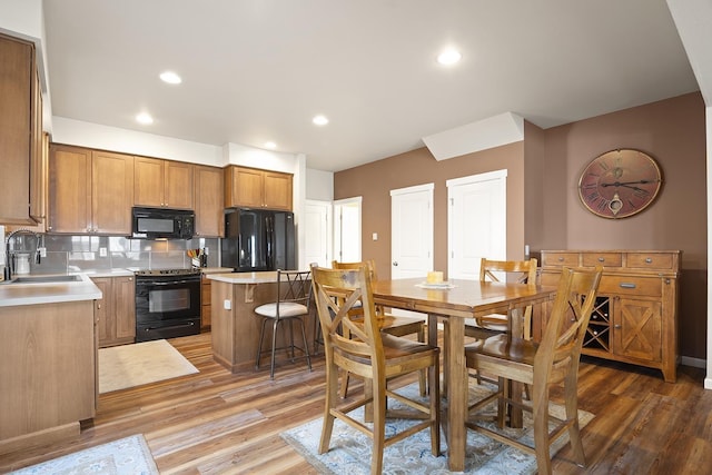 kitchen with a kitchen island, a sink, light wood-style floors, black appliances, and tasteful backsplash