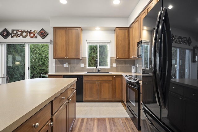 kitchen featuring black appliances, light wood finished floors, a sink, and brown cabinets