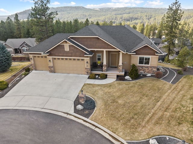 craftsman house with driveway, stone siding, a forest view, an attached garage, and covered porch