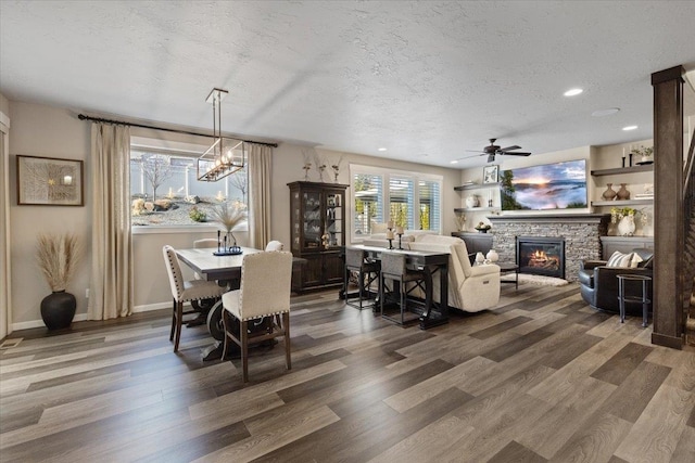 dining area with a textured ceiling, a stone fireplace, wood finished floors, and baseboards