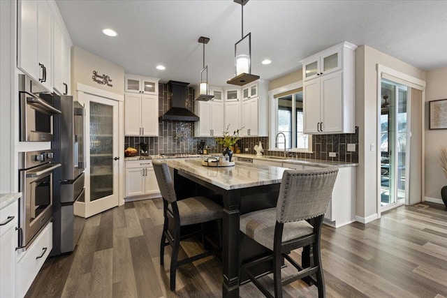 kitchen featuring a breakfast bar area, dark wood-type flooring, a kitchen island, a sink, and wall chimney range hood