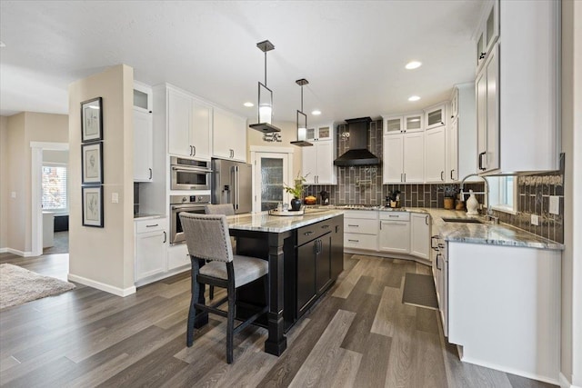 kitchen with a center island, a sink, stainless steel appliances, wall chimney range hood, and backsplash