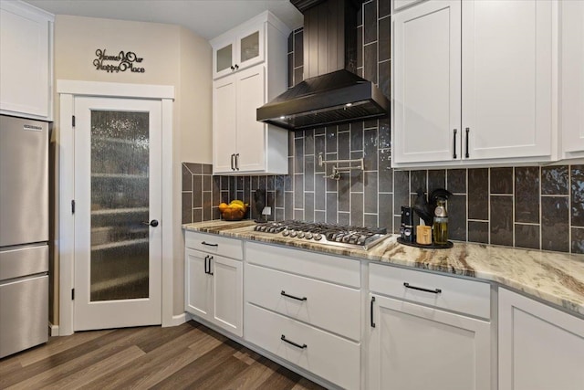 kitchen featuring stainless steel appliances, dark wood-style flooring, white cabinets, wall chimney range hood, and decorative backsplash