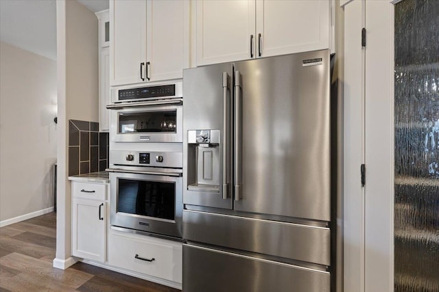 kitchen featuring stainless steel appliances, white cabinetry, backsplash, and dark wood-type flooring