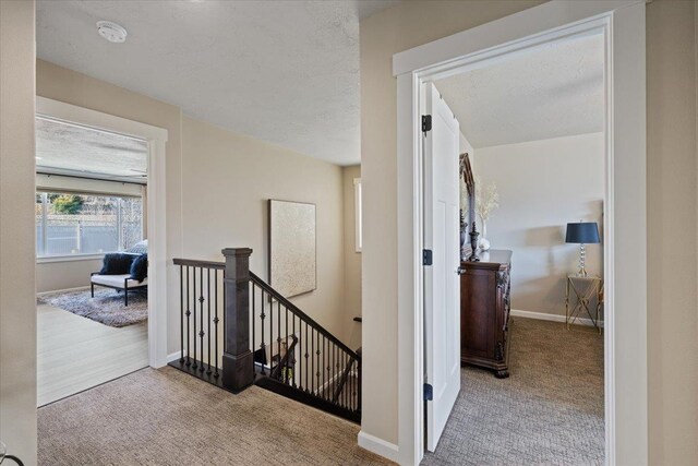 hall with a textured ceiling, carpet, an upstairs landing, and baseboards