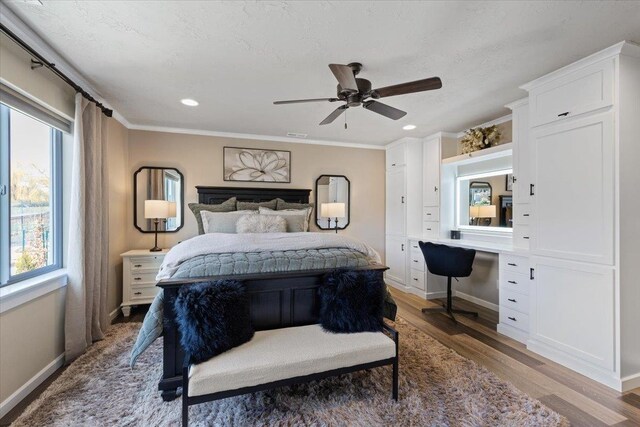 bedroom with ceiling fan, wood finished floors, baseboards, ornamental molding, and built in study area