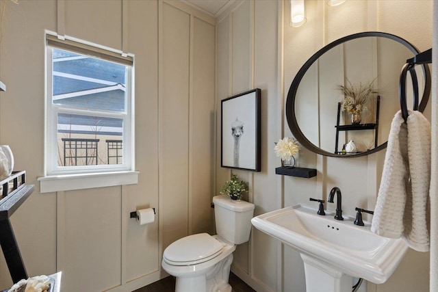 half bath with toilet, a decorative wall, and a sink