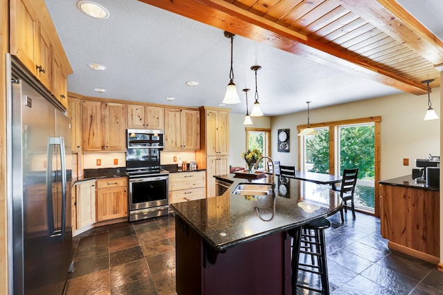 kitchen featuring a breakfast bar, stone tile floors, appliances with stainless steel finishes, a sink, and beamed ceiling