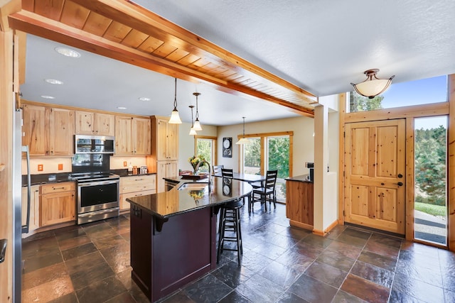 kitchen with stainless steel appliances, dark countertops, stone tile flooring, a sink, and a kitchen breakfast bar