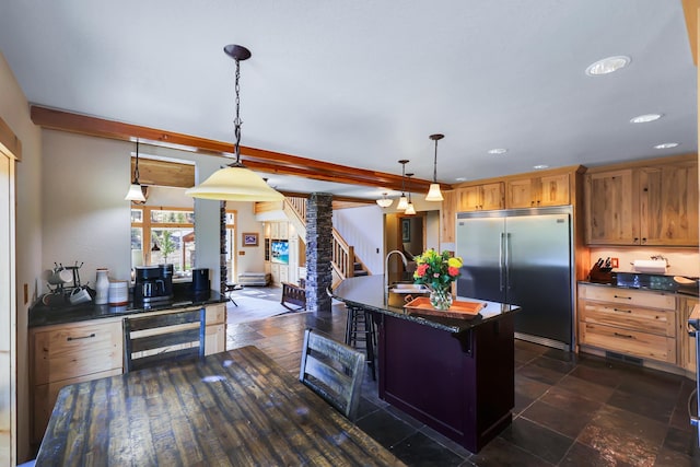 kitchen with pendant lighting, a center island with sink, beverage cooler, built in refrigerator, and a kitchen breakfast bar