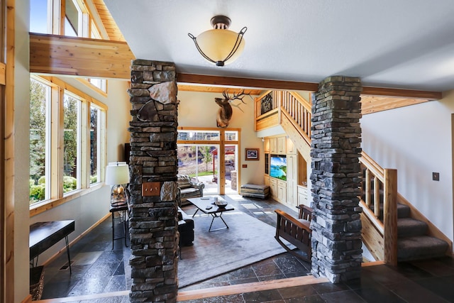 living room with decorative columns, stone tile flooring, beamed ceiling, baseboards, and stairs