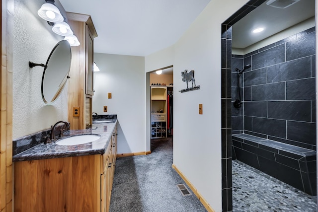 bathroom with double vanity, visible vents, a sink, a tile shower, and baseboards