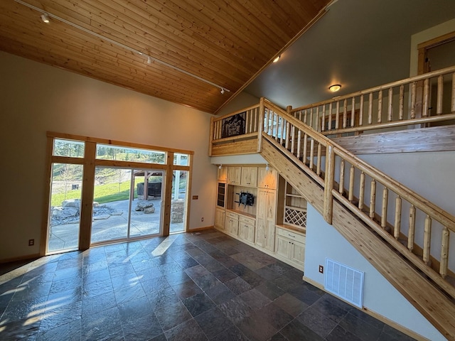 unfurnished living room featuring visible vents, stone tile flooring, baseboards, high vaulted ceiling, and stairway