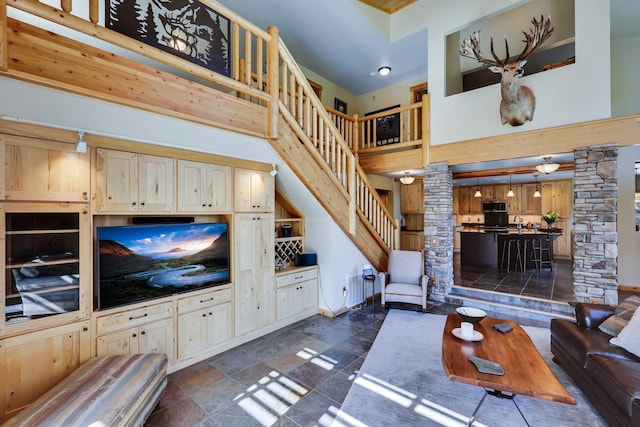 living room featuring stairs, stone tile flooring, a towering ceiling, and ornate columns