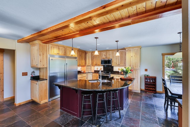 kitchen with beam ceiling, stone tile floors, stainless steel appliances, an island with sink, and baseboards