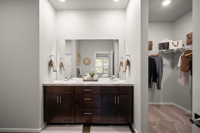 bathroom with double vanity, baseboards, a walk in closet, and a sink