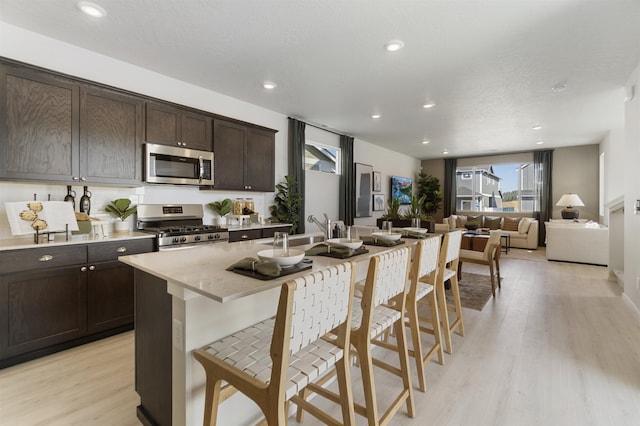 kitchen with stainless steel appliances, dark brown cabinetry, light wood finished floors, and a kitchen breakfast bar