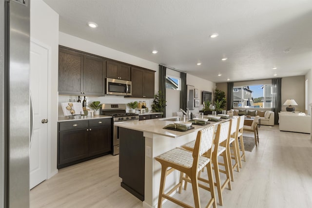 kitchen with a sink, dark brown cabinets, appliances with stainless steel finishes, light countertops, and a kitchen bar