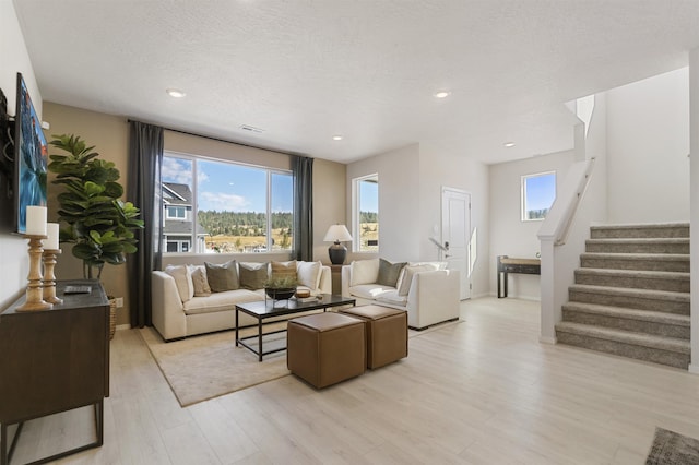 living room featuring a textured ceiling, light wood-style flooring, recessed lighting, visible vents, and stairs