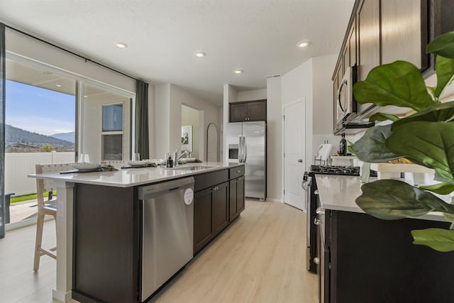 kitchen featuring a kitchen island with sink, light wood-style floors, light countertops, appliances with stainless steel finishes, and dark brown cabinets