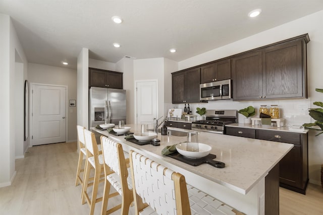 kitchen with dark brown cabinetry, light wood-style flooring, appliances with stainless steel finishes, and a breakfast bar area