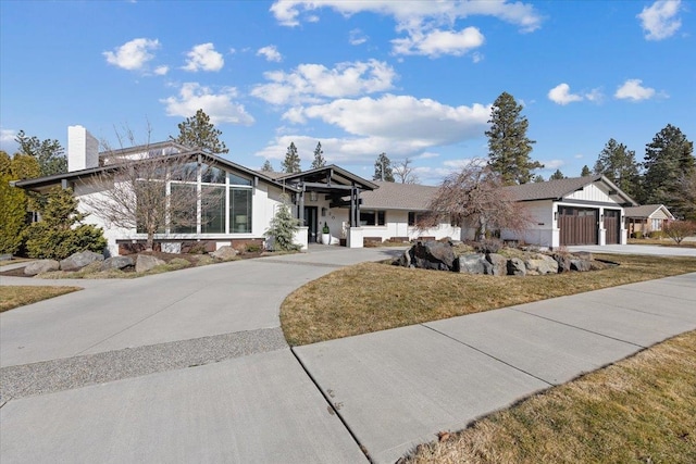 mid-century inspired home featuring an attached garage, a chimney, a front lawn, and concrete driveway