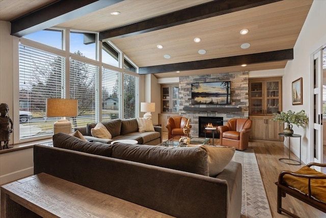 living room featuring a healthy amount of sunlight, vaulted ceiling with beams, a stone fireplace, and wood finished floors