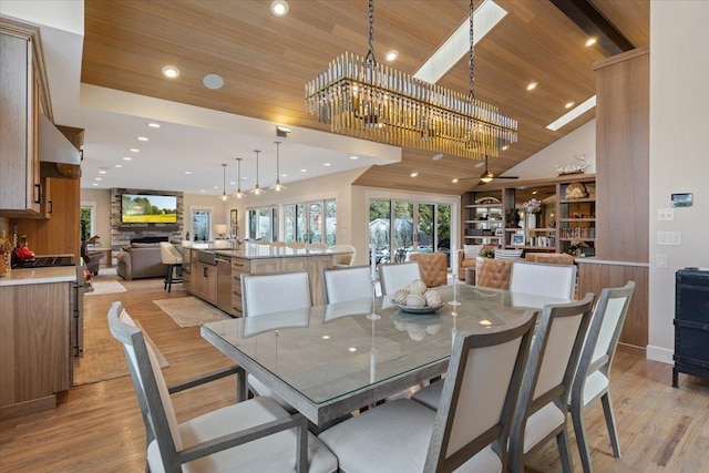 dining area featuring wooden ceiling, recessed lighting, light wood finished floors, and a stone fireplace