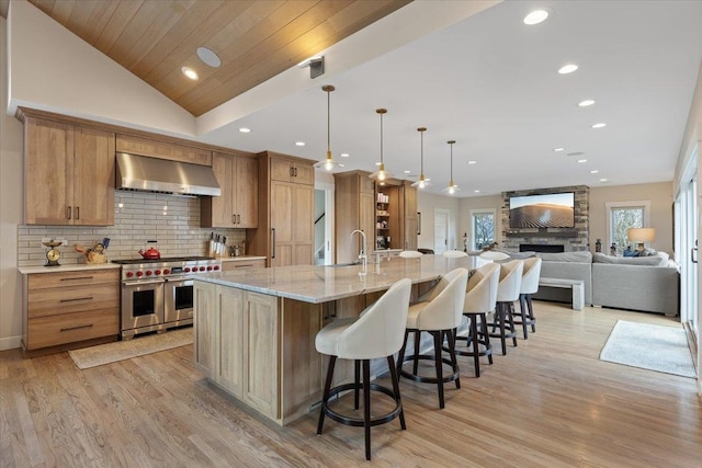 kitchen with range with two ovens, vaulted ceiling, wall chimney range hood, backsplash, and light wood finished floors