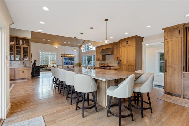 kitchen featuring a spacious island, decorative backsplash, light wood finished floors, and ventilation hood