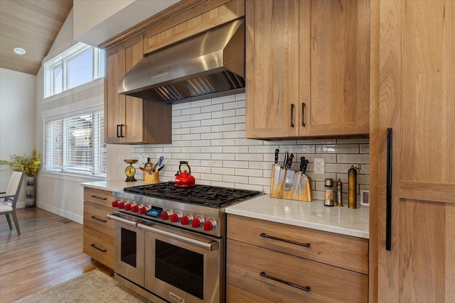 kitchen with tasteful backsplash, range with two ovens, light countertops, light wood-type flooring, and exhaust hood