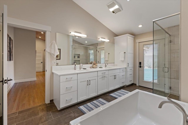 bathroom with double vanity, a freestanding bath, a stall shower, vaulted ceiling, and a sink