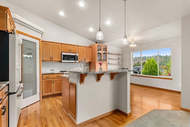 711 W Bolan Ave, Spokane, WA 99224 - kitchen with stainless steel microwave, freestanding refrigerator, a kitchen breakfast bar, glass insert cabinets, and decorative backsplash