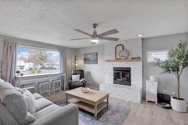 living room featuring a textured ceiling, a fireplace, wood finished floors, and a ceiling fan