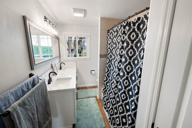 full bathroom with double vanity, curtained shower, a sink, and wood finished floors