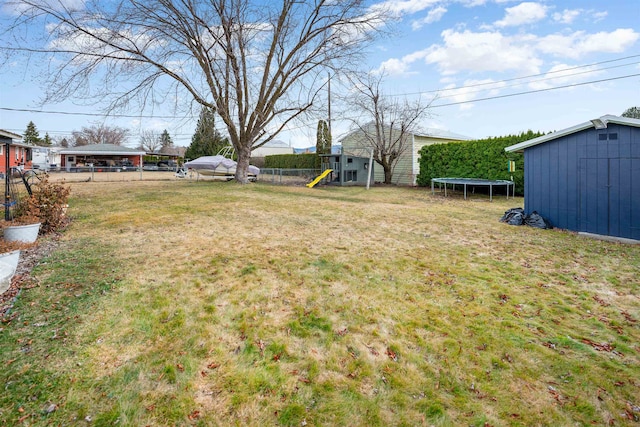 view of yard featuring a trampoline, a playground, a storage shed, fence, and an outdoor structure