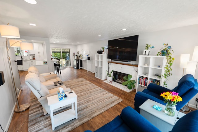 living room featuring a textured ceiling, recessed lighting, wood finished floors, baseboards, and a brick fireplace