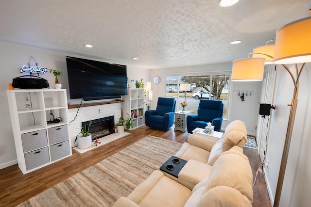 living area with a brick fireplace, a textured ceiling, wood finished floors, and recessed lighting