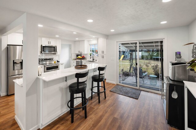 kitchen with appliances with stainless steel finishes, dark wood-type flooring, light countertops, white cabinetry, and a sink