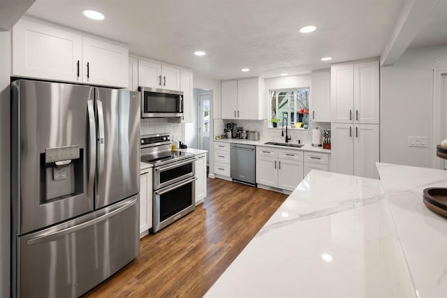 kitchen with tasteful backsplash, dark wood-type flooring, stainless steel appliances, white cabinetry, and a sink